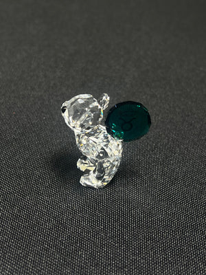 Crystal bear figurine with a green gem on a dark textured surface