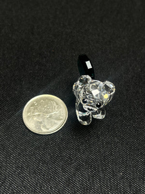 Small crystal bear figurine next to a coin on a black background