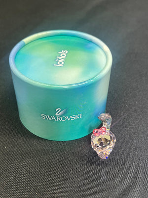 Swarovski crystal heart charm next to a blue Swarovski container on a dark surface