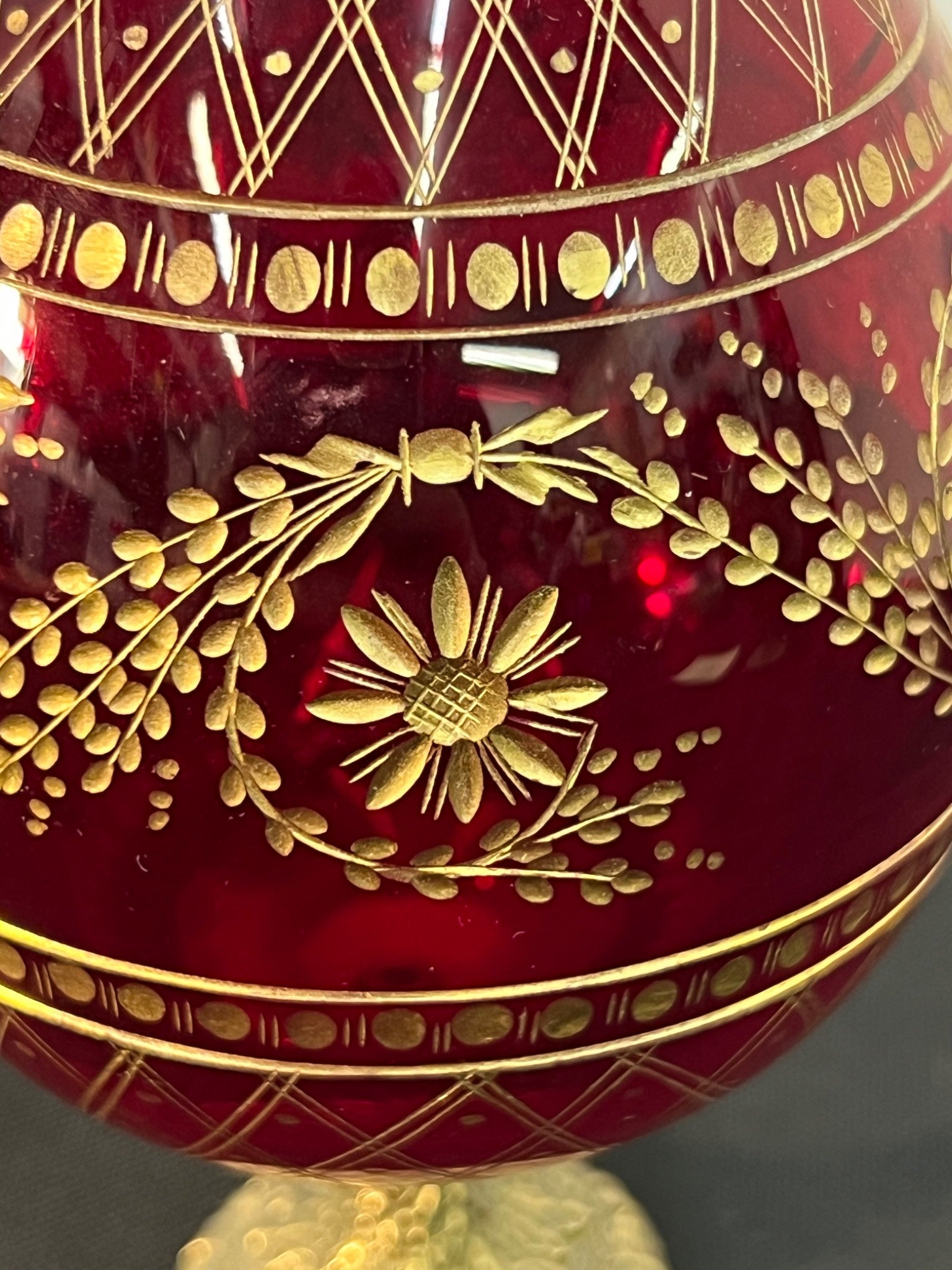 Decorative red glass item with gold floral patterns on a dark background