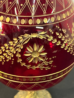 Decorative red glass item with gold floral patterns on a dark background