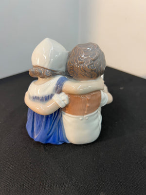 Two figurines hugging on a black surface with a gray background