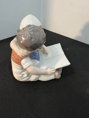 Porcelain figurine of a child reading a book on a black surface.