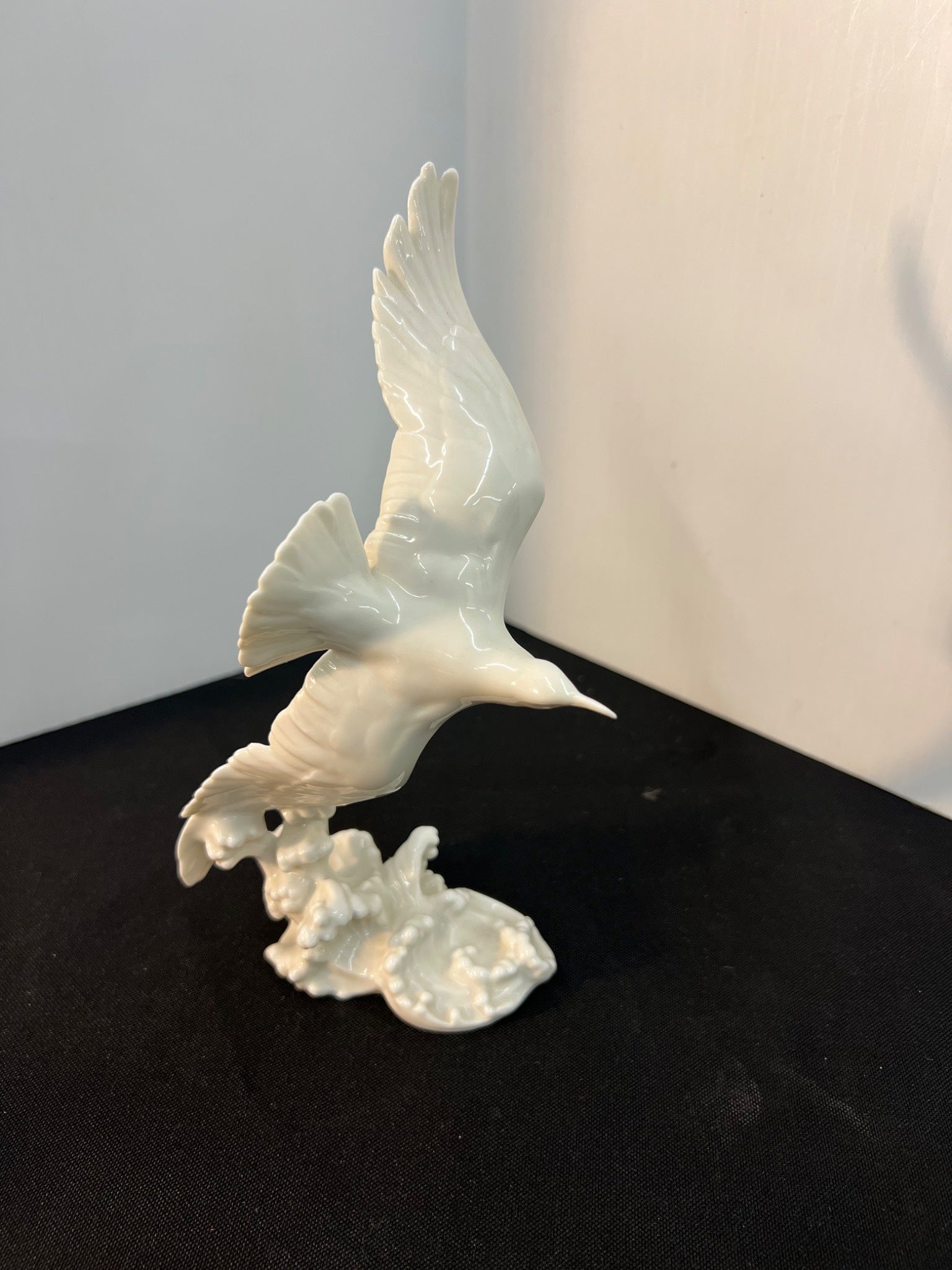 White ceramic sculpture of a bird on a black surface with a light gray background