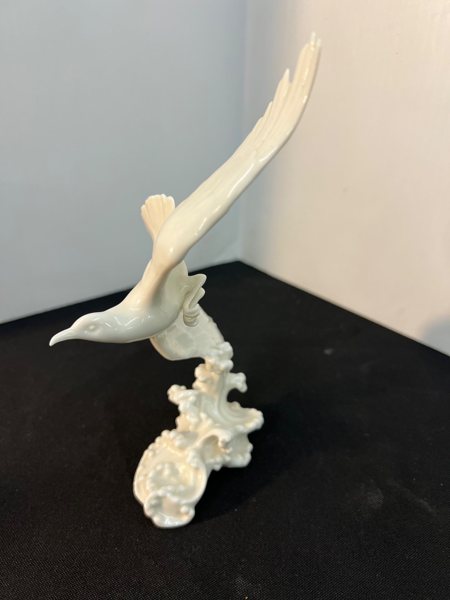 White ceramic sculpture of a bird on a black surface with a white background