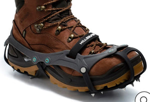 Brown hiking boot with black crampon on a white background
