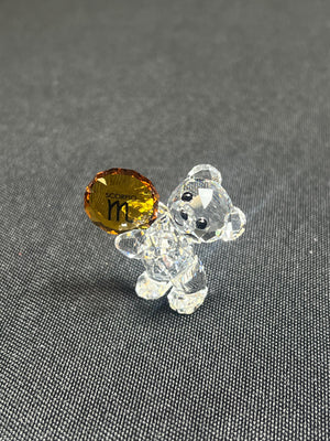 Clear glass bear figurine with a yellow gemstone on a gray background