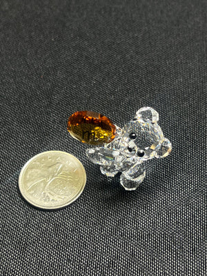 Small crystal bear figurine with a brown gemstone next to a coin on a black background