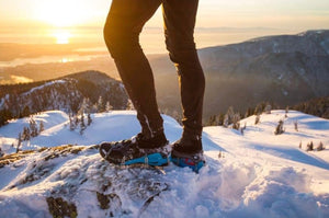 Person snowshoeing on a snowy mountain with a sunset in the background