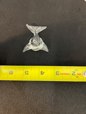 Metallic trident-shaped object on a black background with a yellow measuring tape for scale.