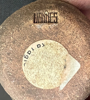 Brown ceramic item with a circular label and text on a textured surface