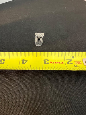 Small clear plastic bear-shaped object on a black surface with a yellow measuring tape.