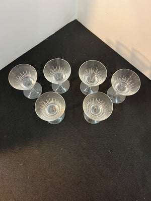 Set of six clear glass candle holders on a black surface.