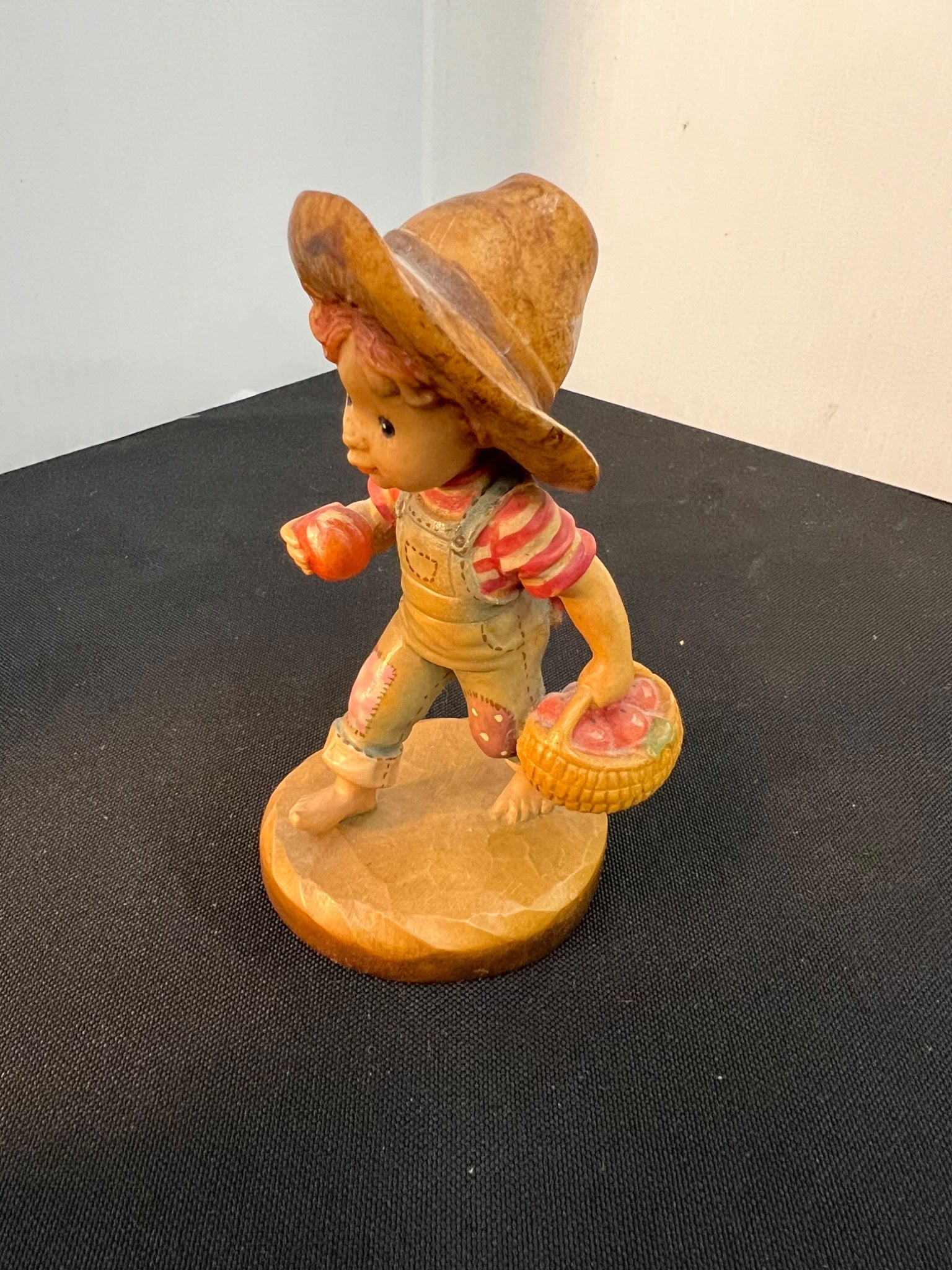 Vintage figurine of a child in a straw hat holding a basket on a black surface.