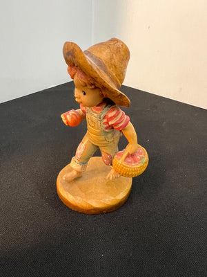 Vintage figurine of a child in a straw hat holding a basket on a black surface.