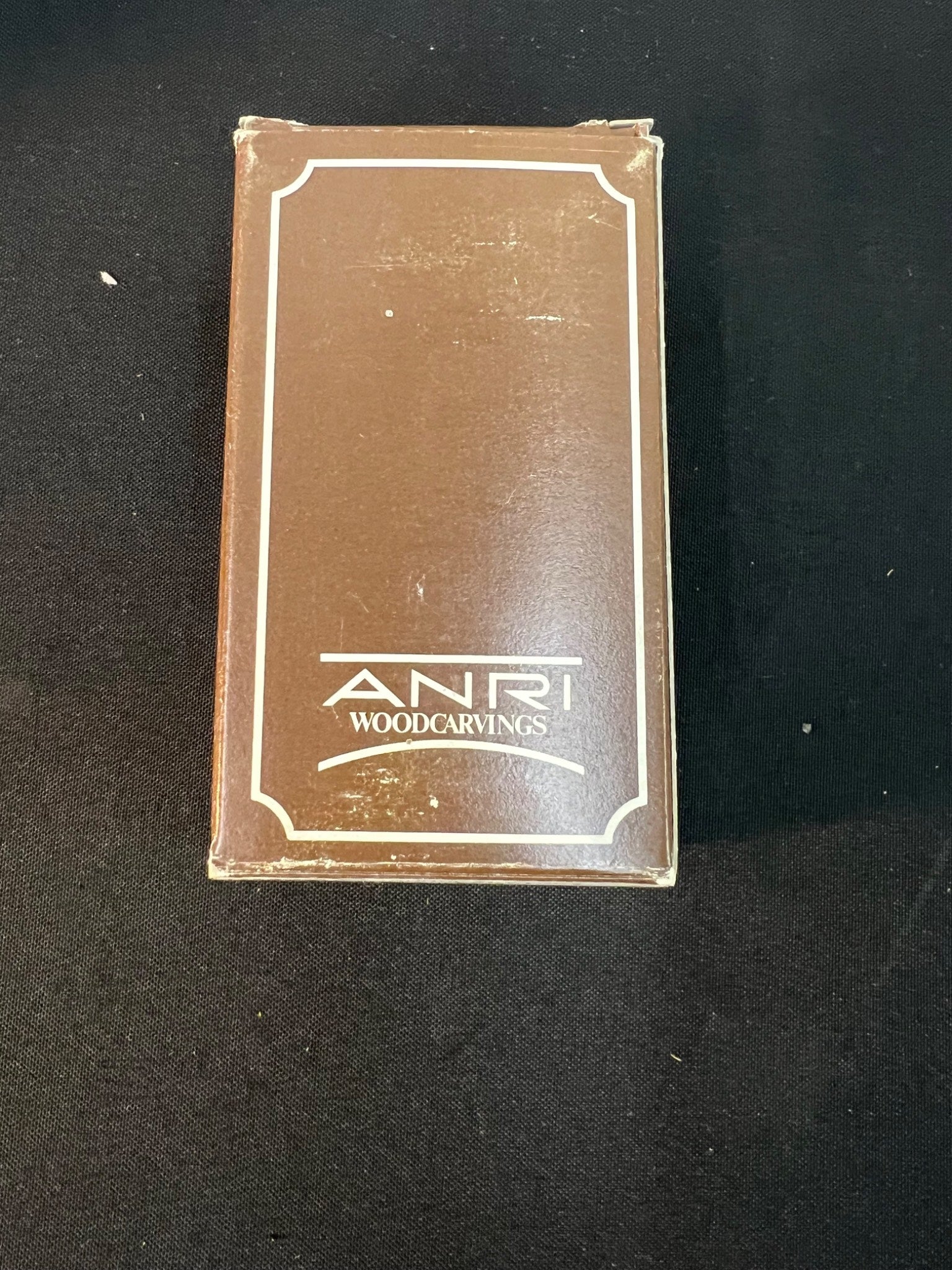 Brown box with 'Anri Woodcarvings' branding on a black background