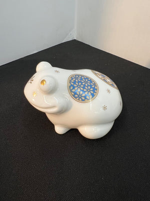 White ceramic piggy bank with decorative blue and gold design on a black surface.