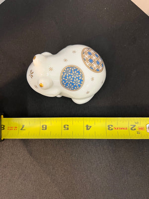 Decorative white figurine with blue and gold patterns on a black surface, measured by a yellow tape measure.