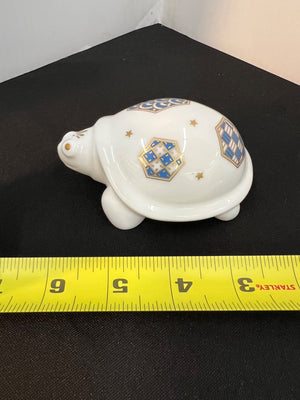 Decorative turtle-shaped object with geometric patterns on a black surface, measured by a yellow tape measure.