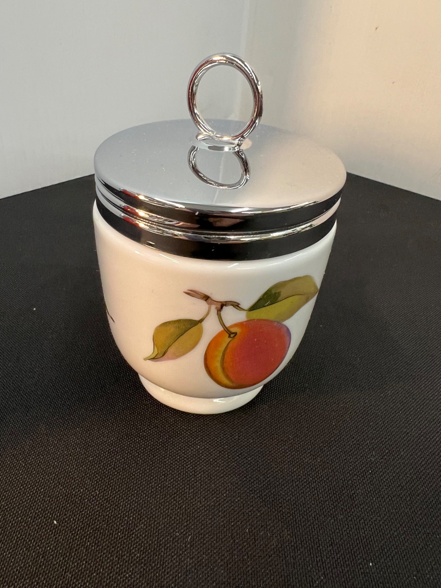 Small ceramic jar with a silver lid and fruit design on a black surface