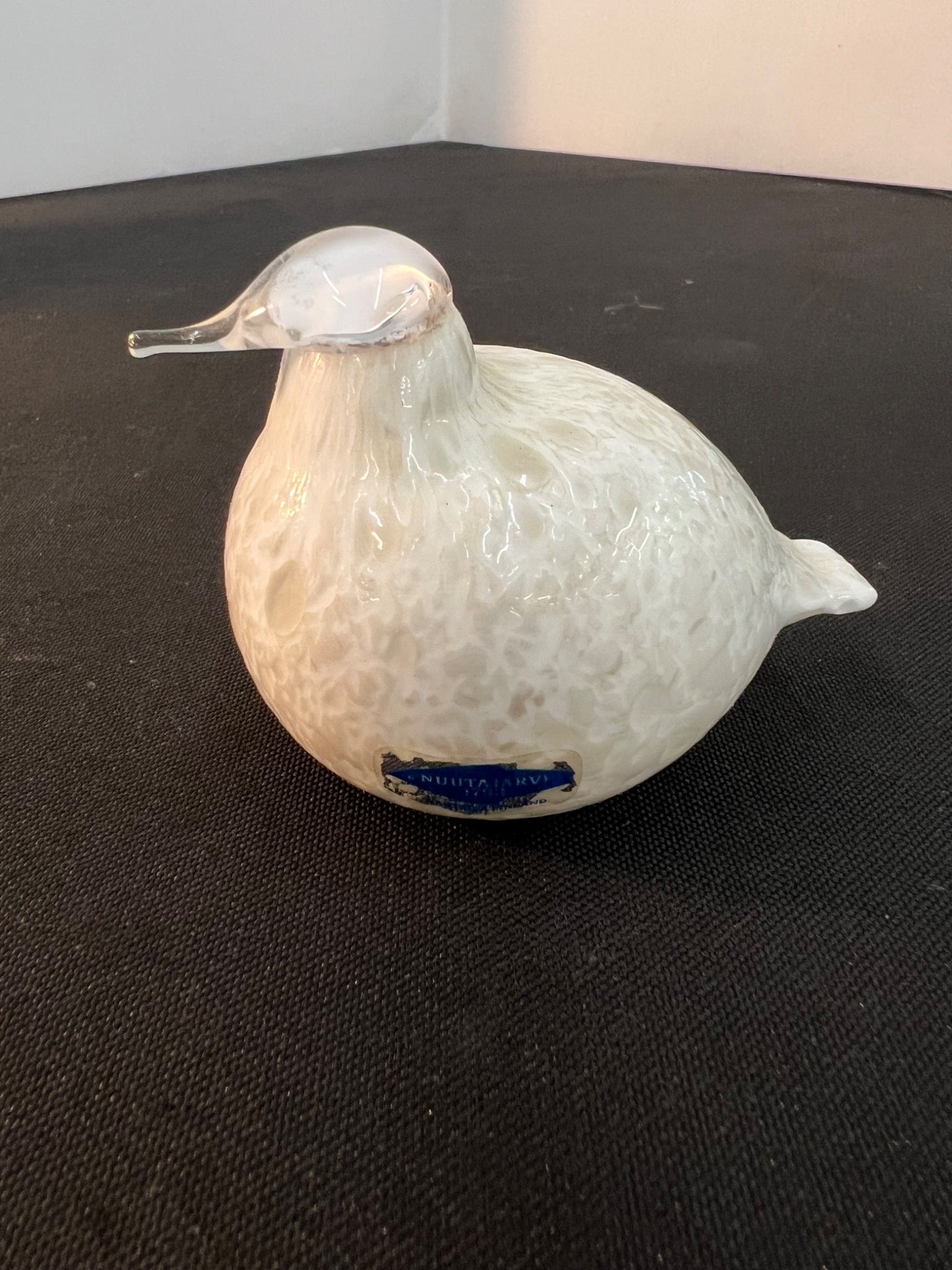 White ceramic duck figurine with a blue label on a black surface