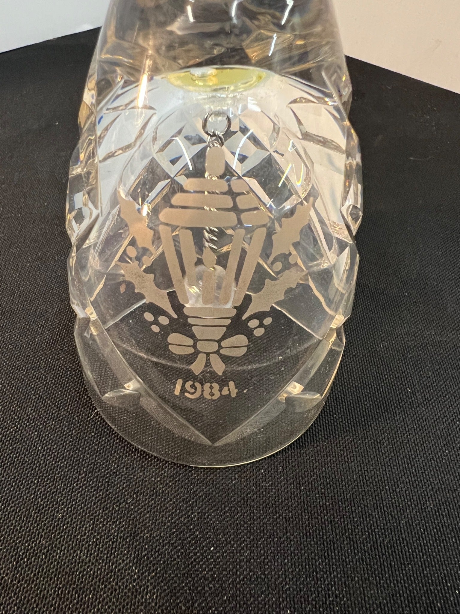 Clear glass ornament with intricate design and '1984' engraving on a black surface