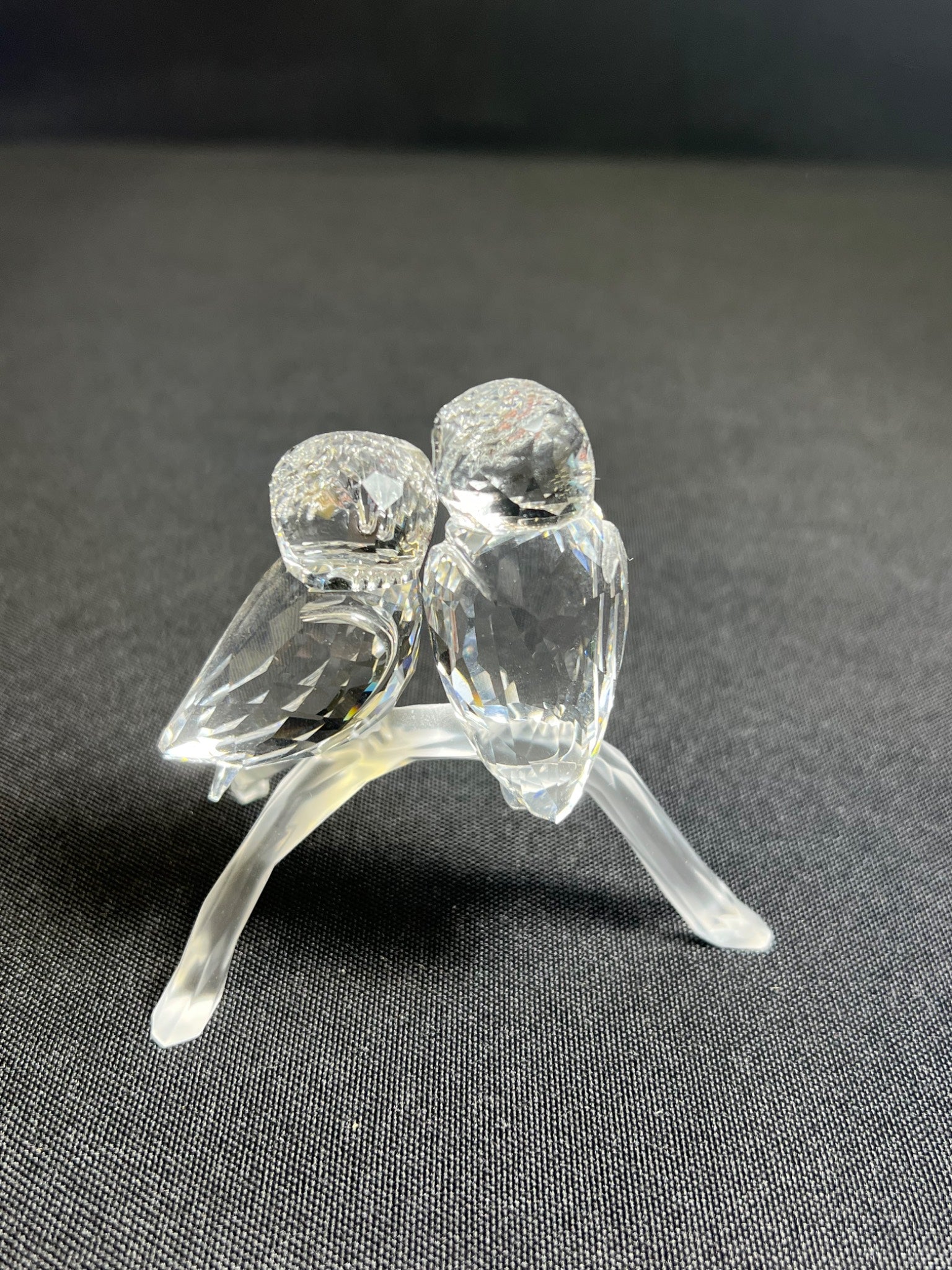 Clear glass figurine of two birds on a stand against a dark background