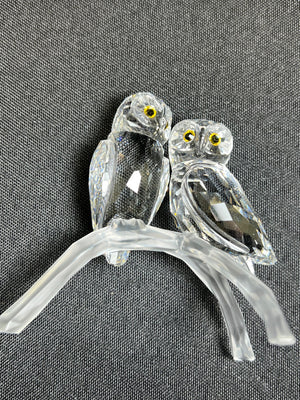 Two glass owls on a branch against a gray background