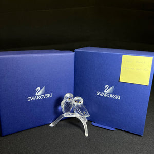Swarovski crystal figurine of two birds in front of blue Swarovski boxes.