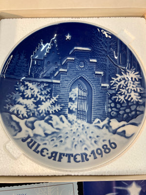 Decorative plate with a winter scene and 'Jule After 1986' text, displayed in packaging.