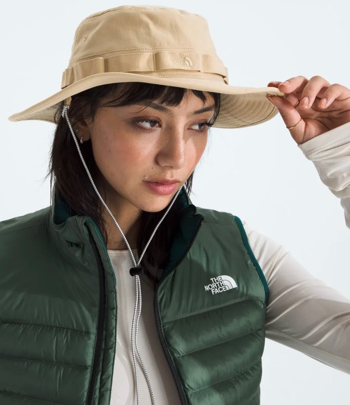 Person wearing a beige hat and green vest with 'The North Face' logo on a light gray background