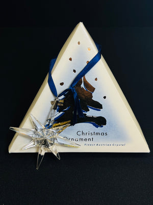 Crystal star Christmas ornament on a triangular box with blue ribbon against a black background