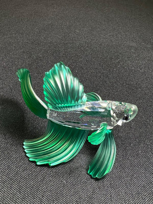 Glass fish figurine with green and clear colors on a dark background