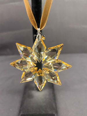 Crystal snowflake ornament on a gold ribbon against a dark background