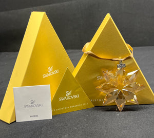 Swarovski crystal Christmas ornament in a pyramid-shaped box on a dark surface.