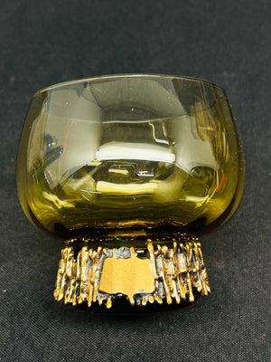 Green glass object with gold base on a dark background