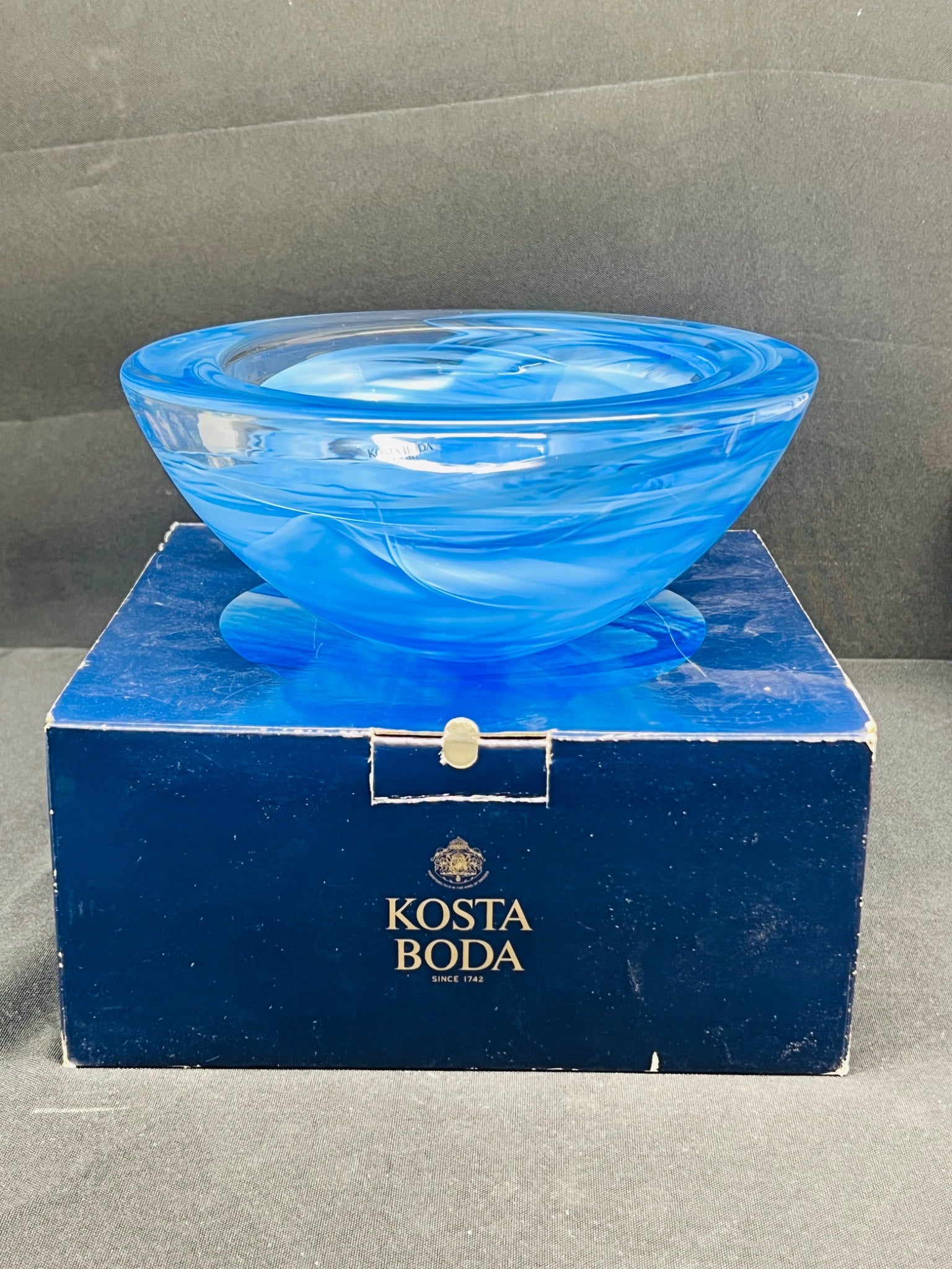 Blue glass bowl on a Kosta Boda branded box against a gray background
