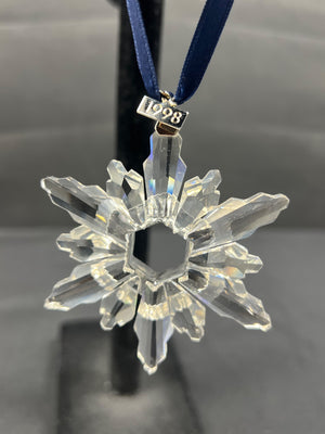 Clear snowflake-shaped ornament with a year tag on a dark background