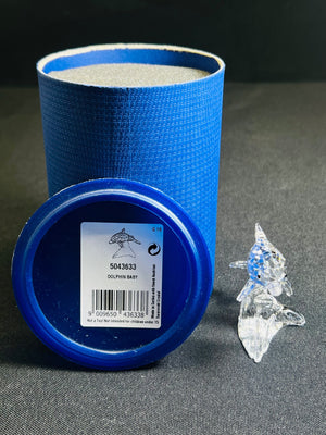 Blue cylindrical container with a label on a gray surface next to a clear crystal figurine.