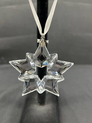 Crystal star-shaped ornament on a black stand against a gray background