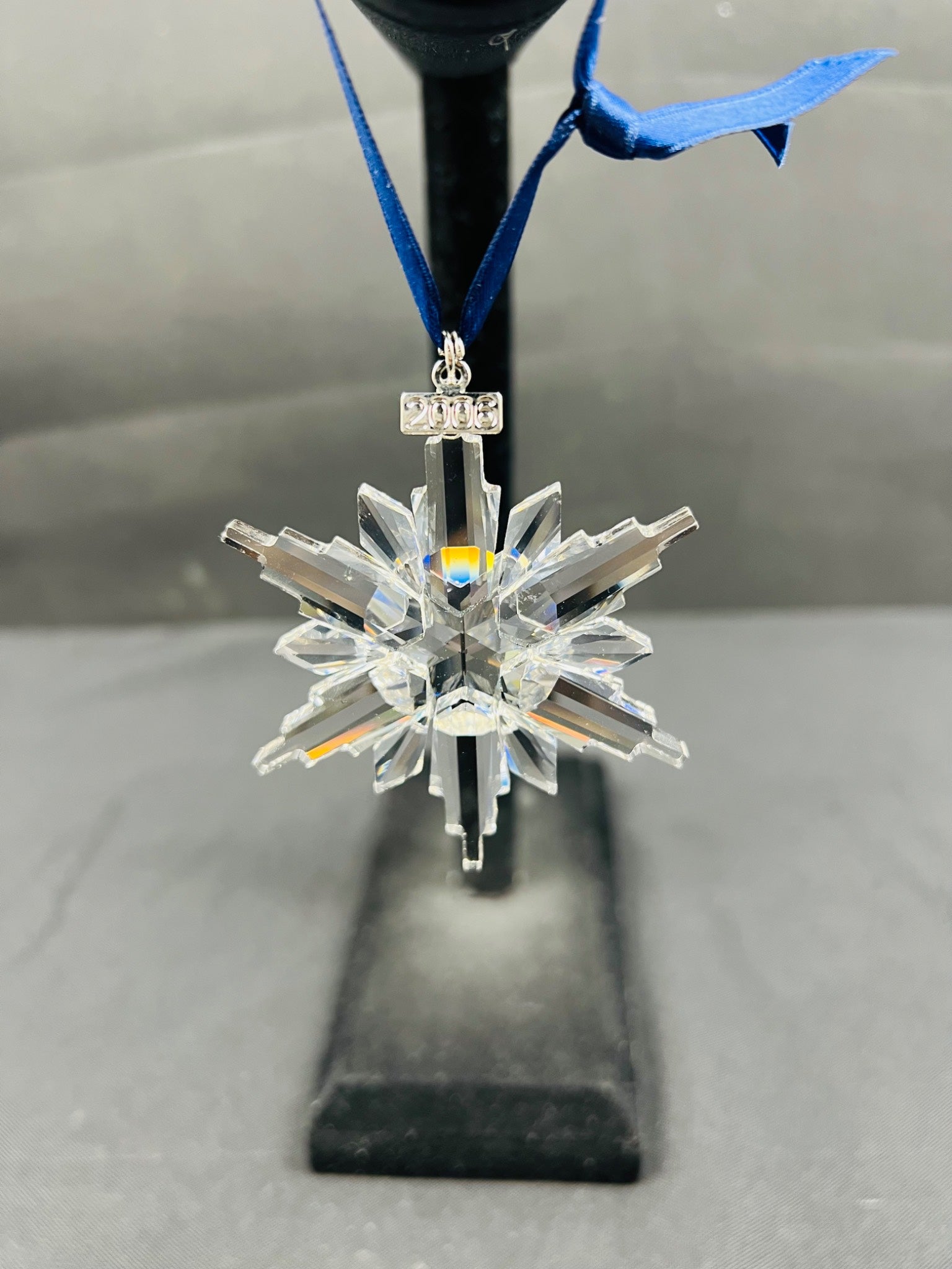 Crystal snowflake ornament on a stand with a blue ribbon against a neutral background
