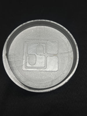 Close-up of a circular metallic object with a central square component on a black background