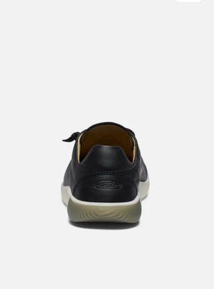 Black leather shoe with white sole on a light gray background