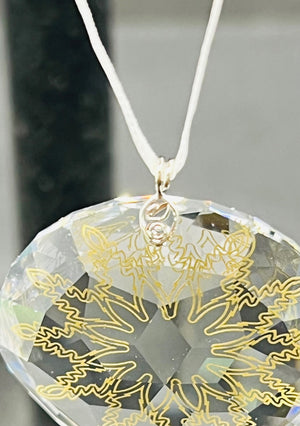 Clear pendant with gold leaf design on a white cord against a blurred background