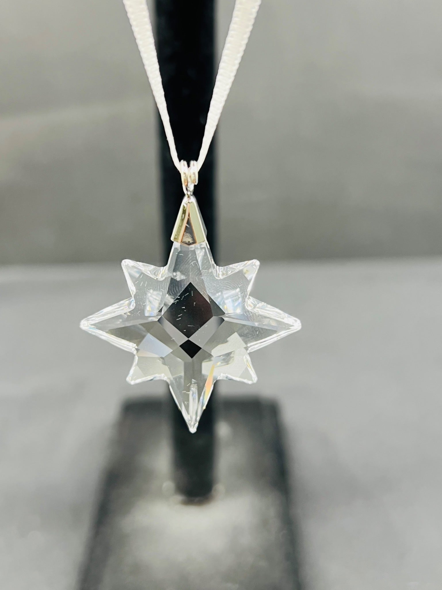 Clear star-shaped pendant on a black stand with a gray background
