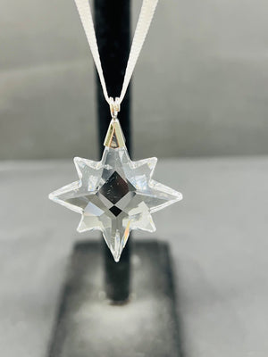 Clear star-shaped pendant on a black stand with a gray background