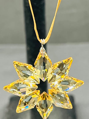 Star-shaped crystal pendant on a gold chain against a neutral background