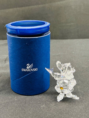 Swarovski branded blue cylindrical container with a clear crystal figurine on a gray surface