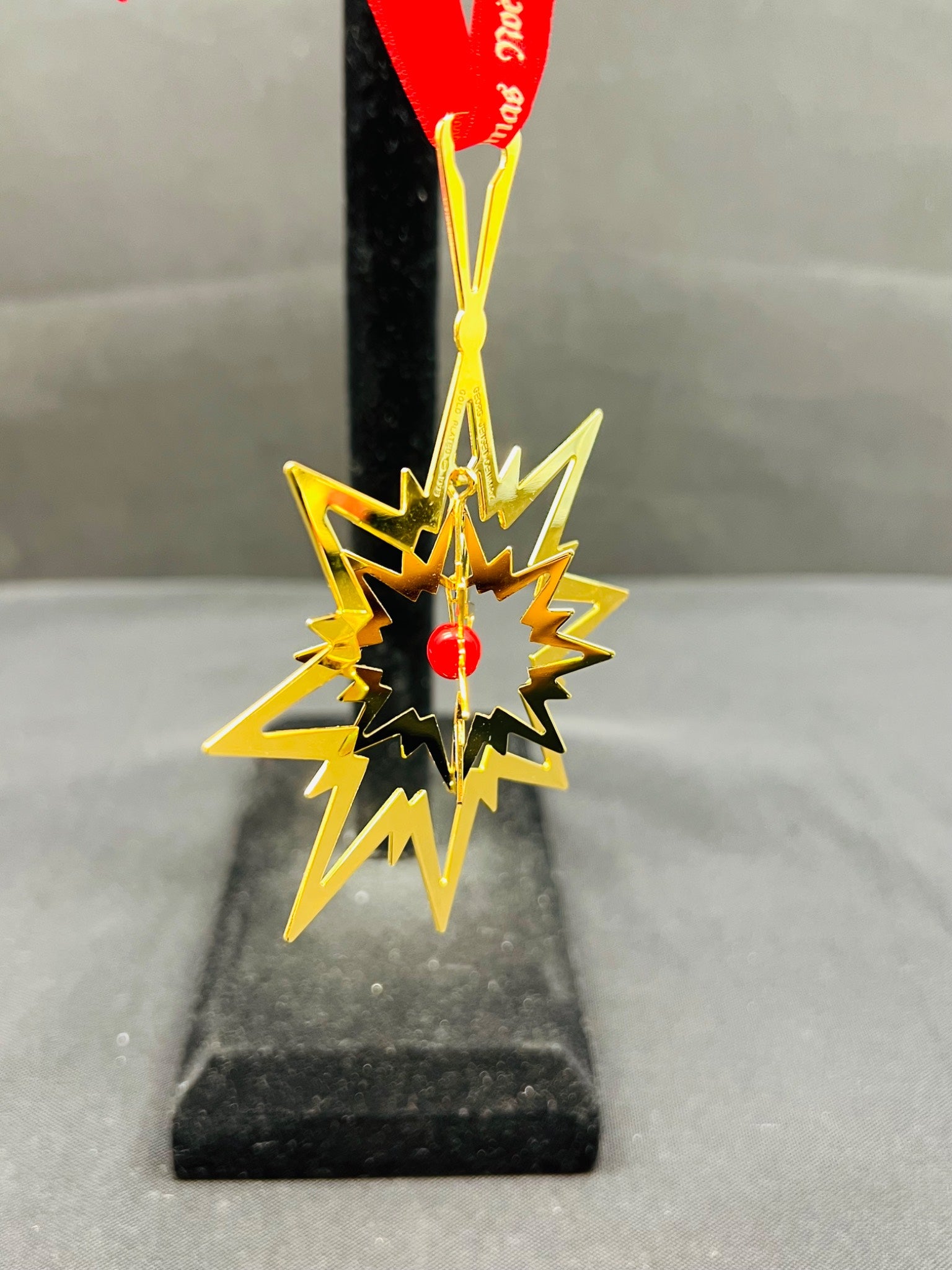 Gold star-shaped ornament on a black stand with a red tag.