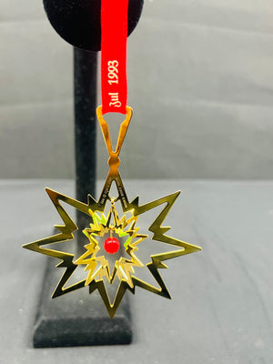 Gold star-shaped ornament with a red center on a stand with a red ribbon.